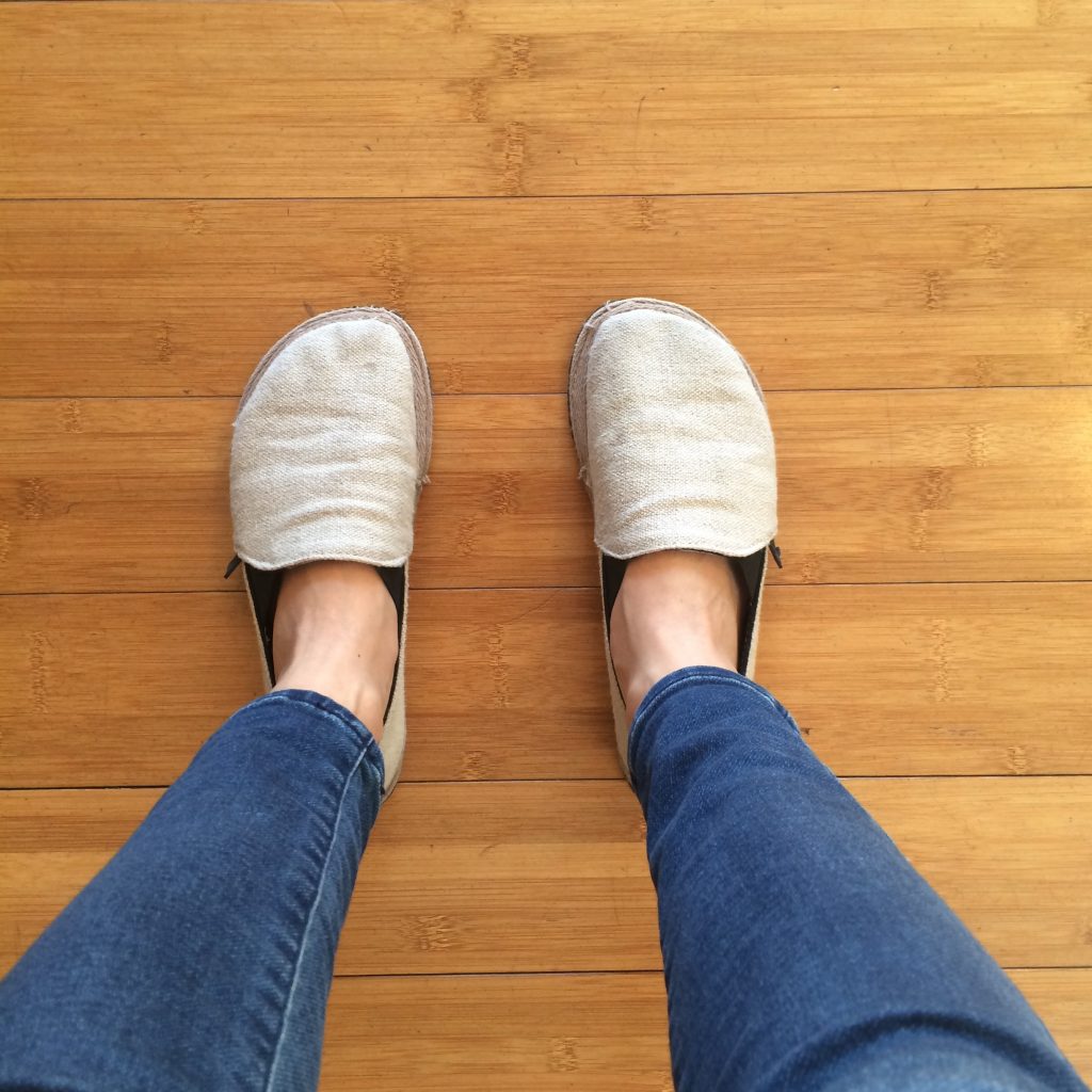 Unshoes Footwear Terra Vida canvas hemp barefoot slip on shoes shown on a pair of feet standing on wood