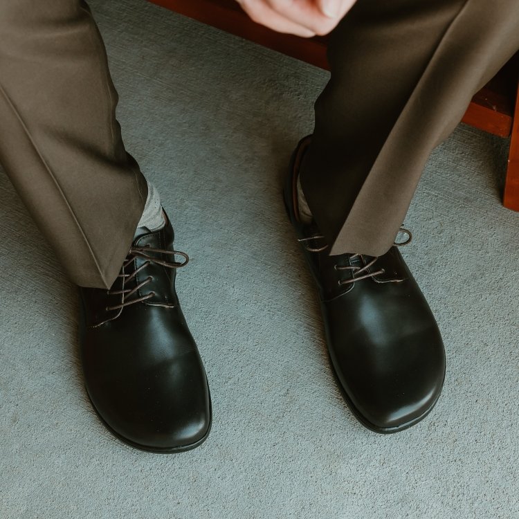 A cropped shot of a man in dress clothes from the knee down. He has Zaqq Peaq barefoot dress shoes on his feet. 