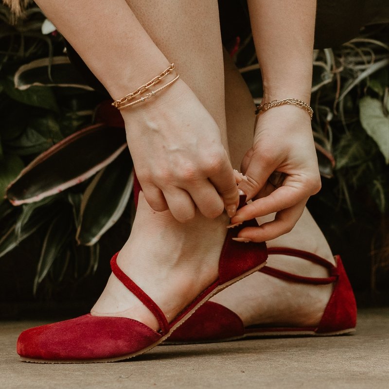 Shapen Orchid in red being put on a pair of feet. The front foot is lifted off the ground highlighting the flexible zero drop outsole