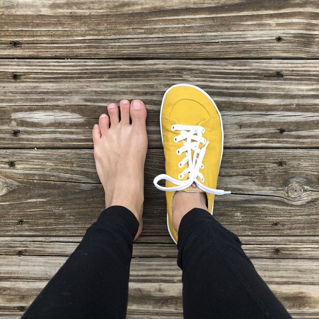 a top down image of a pair of feet with one foot bare and the other wearing mukishoes barefoot sneakers, a review showing that they are shaped like feet.