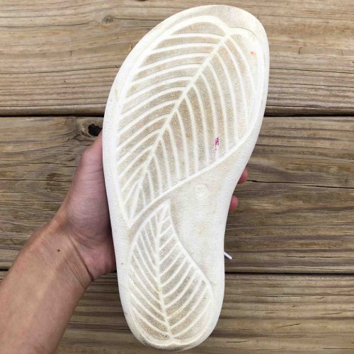 Belenka Barefoot Prime sneaker in white close up of outsole held in one hand over a wood patio