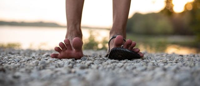 a close up image of a person's feet with toes splayed upward, with one foot barefoot and the other in an earth runners elemental tribal print sandal