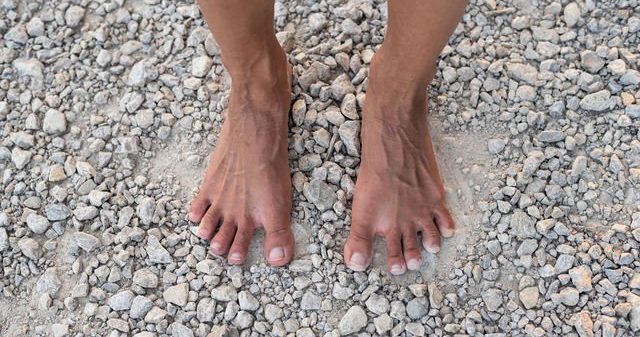 a close up town down shot of two bare feet standing on loose gravel with toes spread and muscles showing.