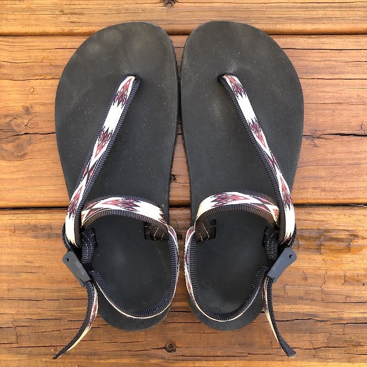 a top down view of a pair of elemental Earth Runners sandals with a tribal strap, over a wood floor