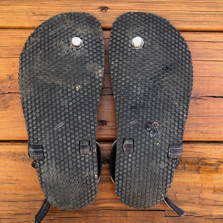 a top down view of a pair of Elemental Earth Runners sandals with a tribal strap, upside down with outsoles facing up over a wood floor