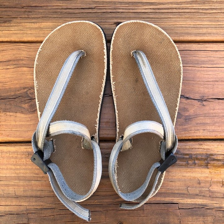 a top down view of a pair of Alpha Earth Runners sandals with a charcoal strap and cotton footbed, over a wood floor