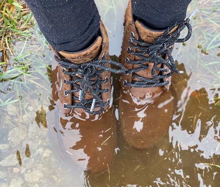 a close up of a pair of feet standing in a puddle of water wearing lems umber brown waterproof boulder boots