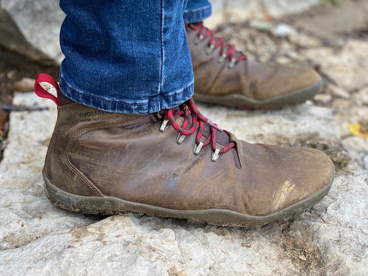 A side view of a pair of feet wearing the Vivobarefoot Tracker barefoot hiking boot, standing on rock outdoors