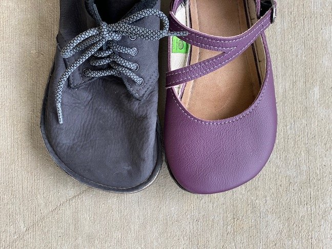 a top down view of two softstar barefoot shoes next to each on concrete. On the left is the Primal Sawyer in black and the primal Merry Jane in elderberry