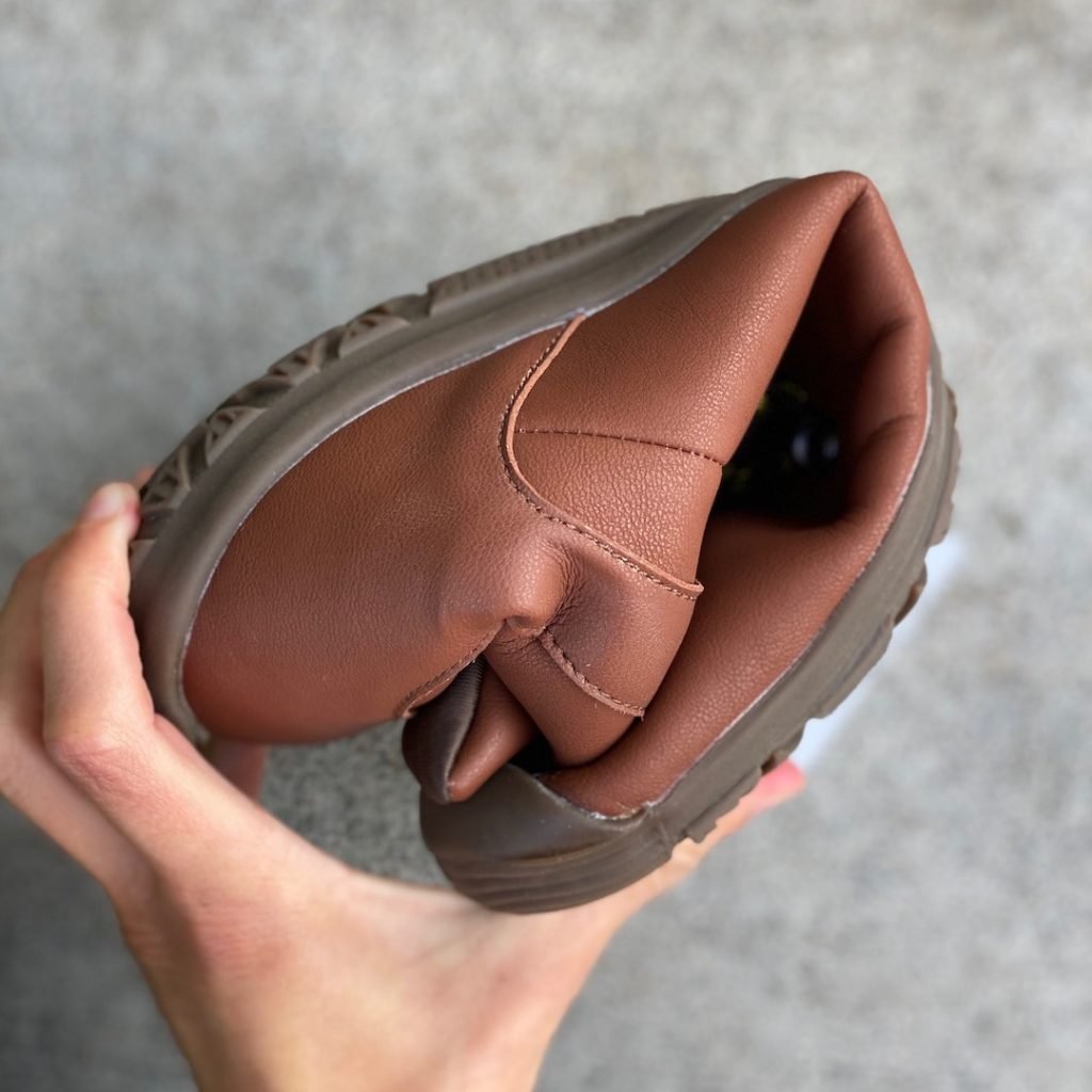 a close up of a hand holding a rolled up vegan freet mudee in brown for the best barefoot minimalist hiking boots review