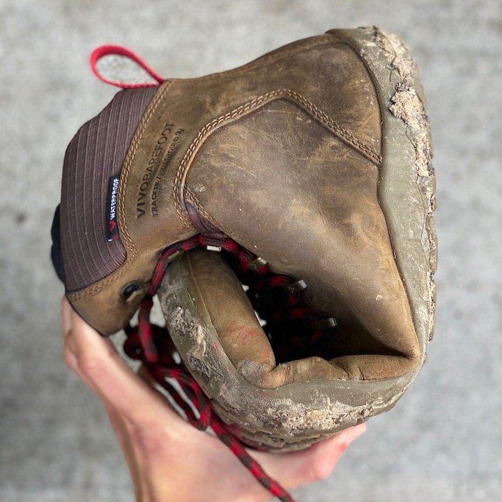 a close up of a hand holding a rolled up vivobarefoot tracker in brown