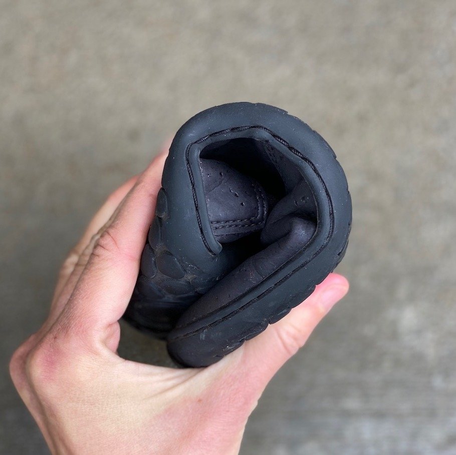 a hand holding a rolled up vegan barefoot chelsea boot from Mukishoes made from black cork