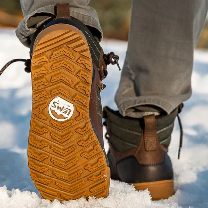 A close up view of the outsole of a pair of Lems Outlander wide toe box hiking boots outside in snow