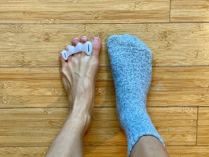 a top down view of a pair of feet wearing Correct Toes. One foot is bear and the other is wearing a barefoot socks