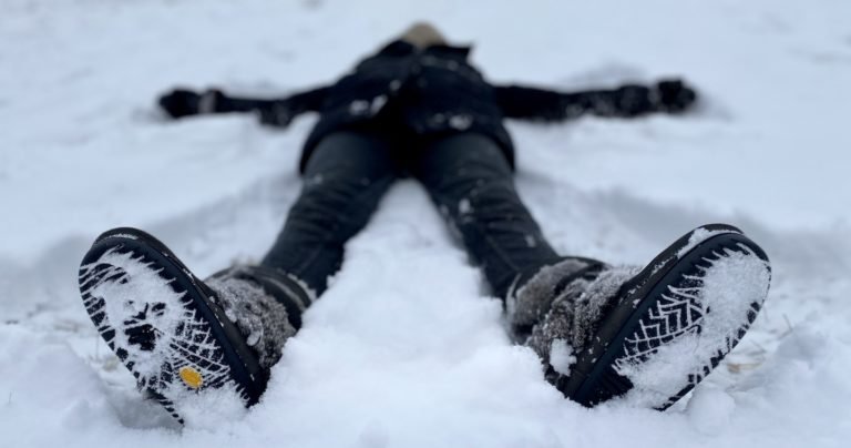 A blurry figure laying on their back in the show, wearing Manitobah Mukluks winter boots, showing the snowy vibram outsole bottoms