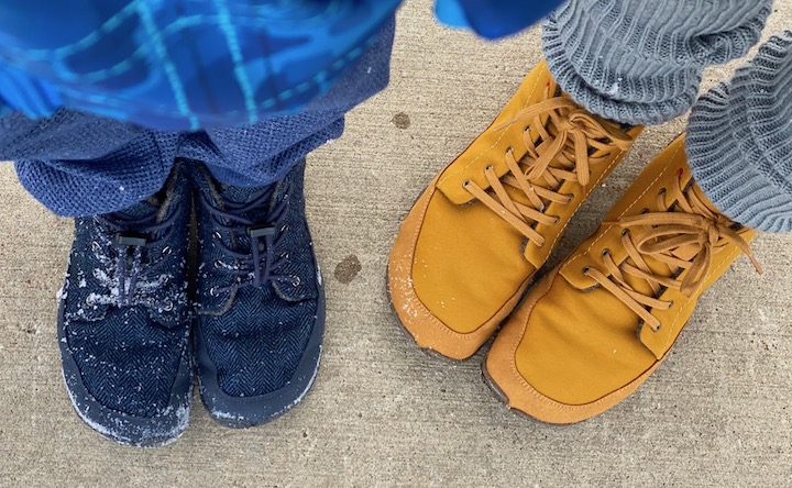 A top down view of two pairs of feet standing in snow covered wildling shows. One is a child wearing the Nessie, and the other is an adult wearing the Honeybear.