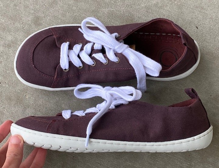 A pair of plum barefoot sneakers from Mukishoes. One sneaker is turned sideways to show the completely flat sole and the other shows the foot shaped top.