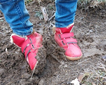 A little boy's leg wearing Ten Little Everyday High Top shoes standing in mud.