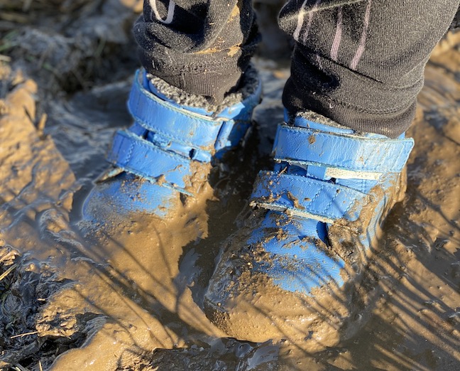 A kid wearing Be Lenka Penguin Boots standing in very mucky mud