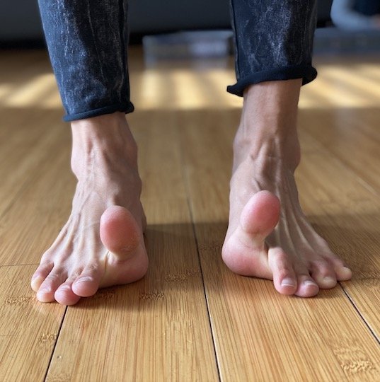 A close up of a woman's feet doing foot exercises. Her big toes are raised in the air while her other toes remain on the floor.