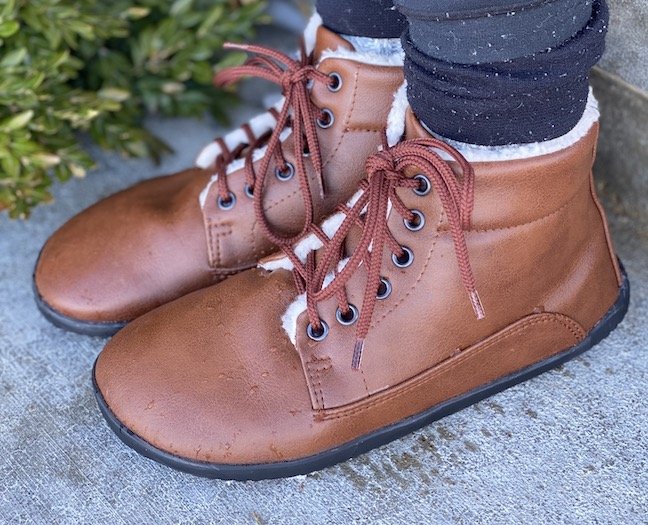 A woman's feet wearing Ahinsa Winter vegan barefoot boots outside standing on concrete. Water drops are on the toes of the boots.