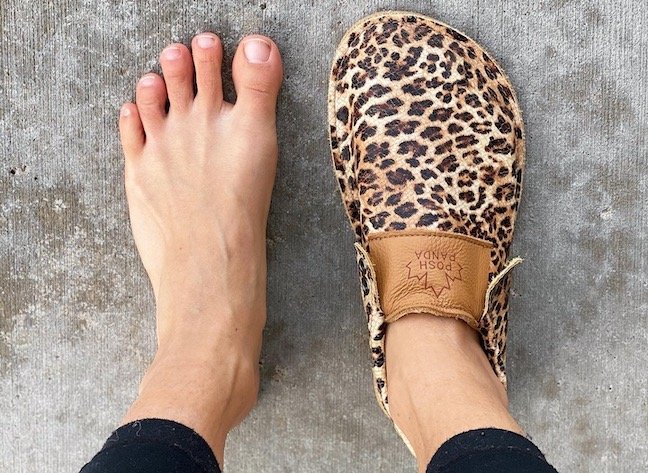 Close up of a woman's feet with one Posh Panda Moccasin on her right foot, her left foot is bare to show how they are foot shaped.