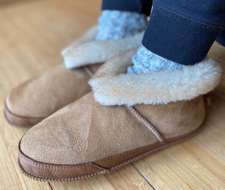 An angled view of a woman's feet staying cozy in a pair of Softstar handmade sheepskin Fireside slippers.