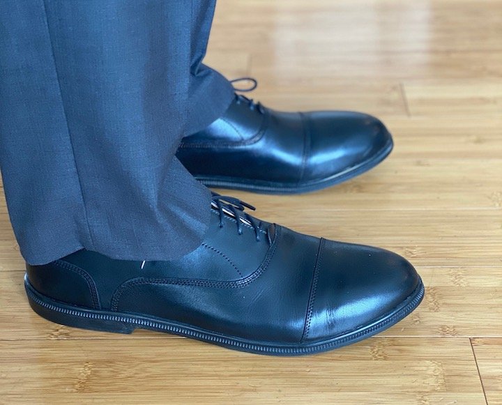 A close of up a man's legs wearing dress pants and a pair of Caret's dress shoes in black leather