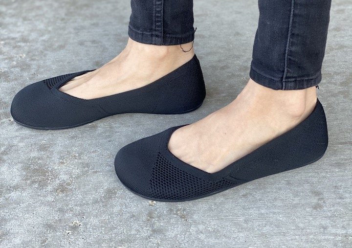 A woman's feet close up wearing a pair of Xero Shoes black knit rothy's dupe barefoot flats.