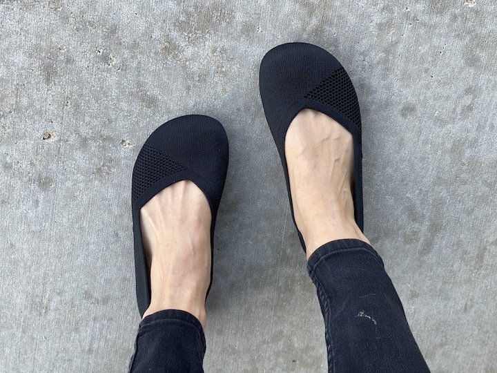 A top down view of a woman in black skinny jeans wearing black knit Phoenix zero drop flats from Xero shoes.