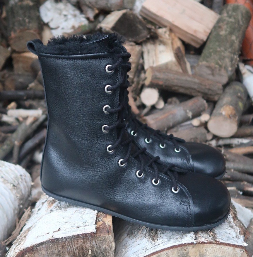 A close up side view of a pair of Zlatush combat boots sitting on a log pile. They are zero drop, lace up, with a wide toe box