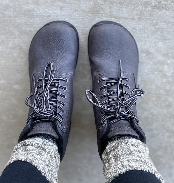 A top down view of a pair of legs wearing feelgrounds patrol vegan barefoot winter boots with socks sticking out the top over black leggings.