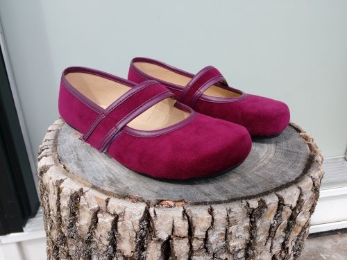 A close up of a pair of velvet vegan burgundy Ballet Pumps by tadeevo sitting unworn on a tree stump.