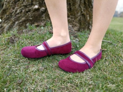 A close up of a woman's legs wearing Tadeevo burgundy velvet ballet pumps standing by a tree in the grass.