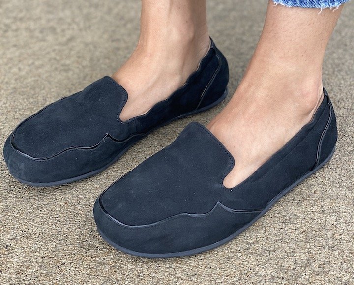 Top side angled photo of a woman's feet in Lisbeth Joe London black suede barefoot loafers with decorative piping to disguise width.