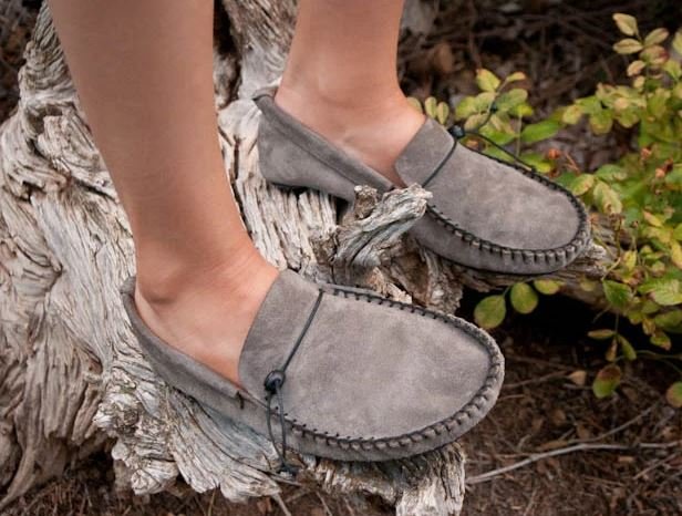 Stock photo of a person's feet standing on a tree in Unshoes Forager, a suede moccasin style slip on with an extra wide toe box.