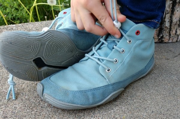 Close up of Wildling Pegasus being put on by a child. The gray outsole on one shoe is visible and the other elastic laces are being cinched.