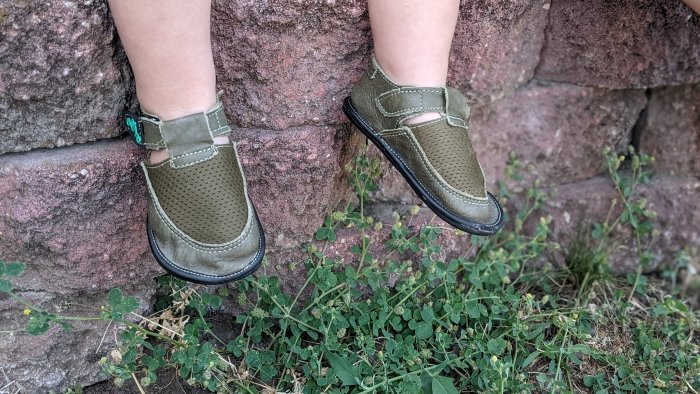 Magical Shoes Bebe on wide toddler feet. The child's feet are in front of a red stone wall