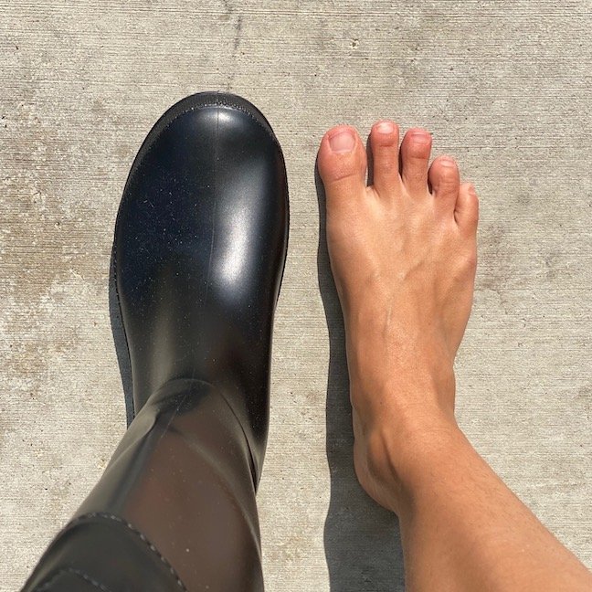 Top down view of a woman with one Asgard rain boot on and one barefoot