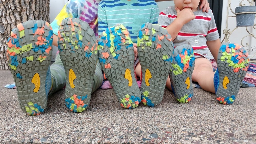 3 kids sitting on their front stoop with legs extended in front of them. The soles of their inexpensive Saguaro shoes are in the forefront of the photo.