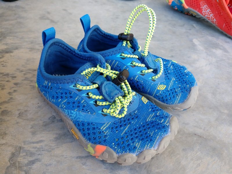 Front angled view of Saguaro cheap barefoot sneakers in toddler size showing the elastic laces looped around on one shoe, and left sticking up on the other.