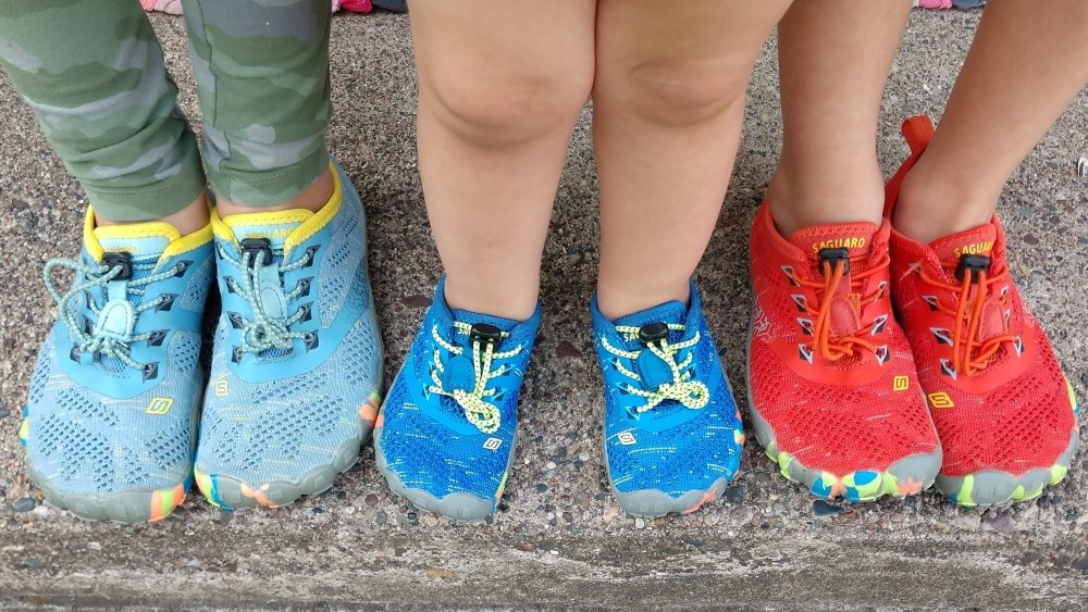 Top down view of 3 children's feet in Saguaro inexpensive Amazon shoes that are barefoot friendly.