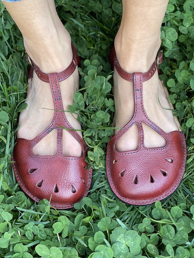 A close up of a pair of feet standing in grass wearing Garnet Tarian barefoot ballet flats from Gea Soles