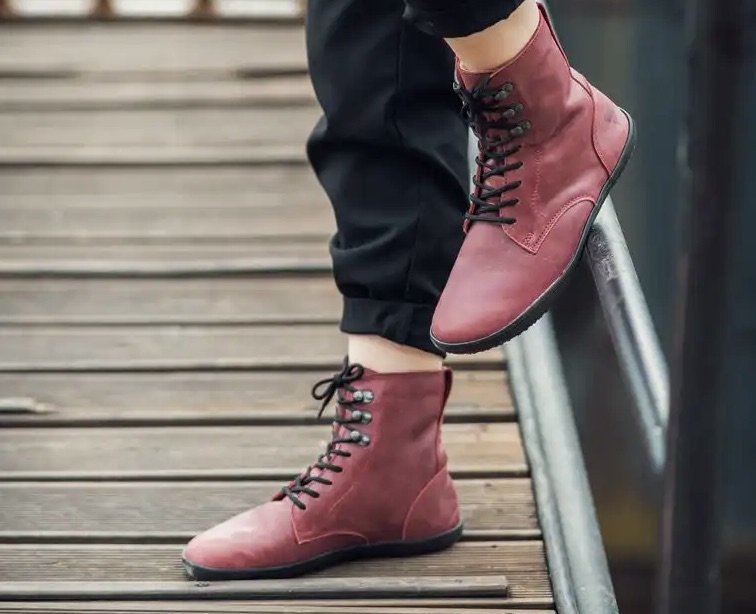 Stock lifestyle image of Angles Fashion zeus barefoot lace up combat style zero drop boots in Burgundy with red soles and laces.