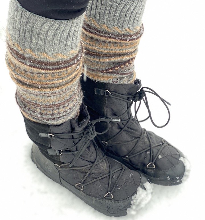 Front angled view of Be Lenka Snowfox boots being worn with thick Knitido wool toe socks standing outside in the snow. Black lace up zero drop warm winter snow boots with an extra wide toe box.