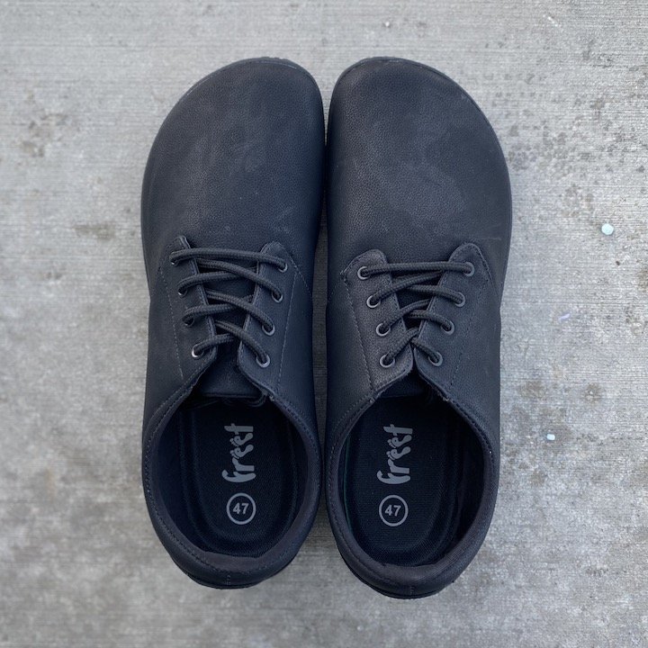 a close up of a pair of Freet barefoot shoes vegan Citee sneakers in black sitting on pavement