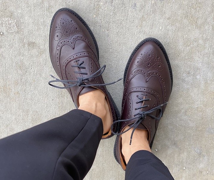 A top down view of a pair of feet wearing the Carets Victoria Wingtip in Oxblood standing on Concrete