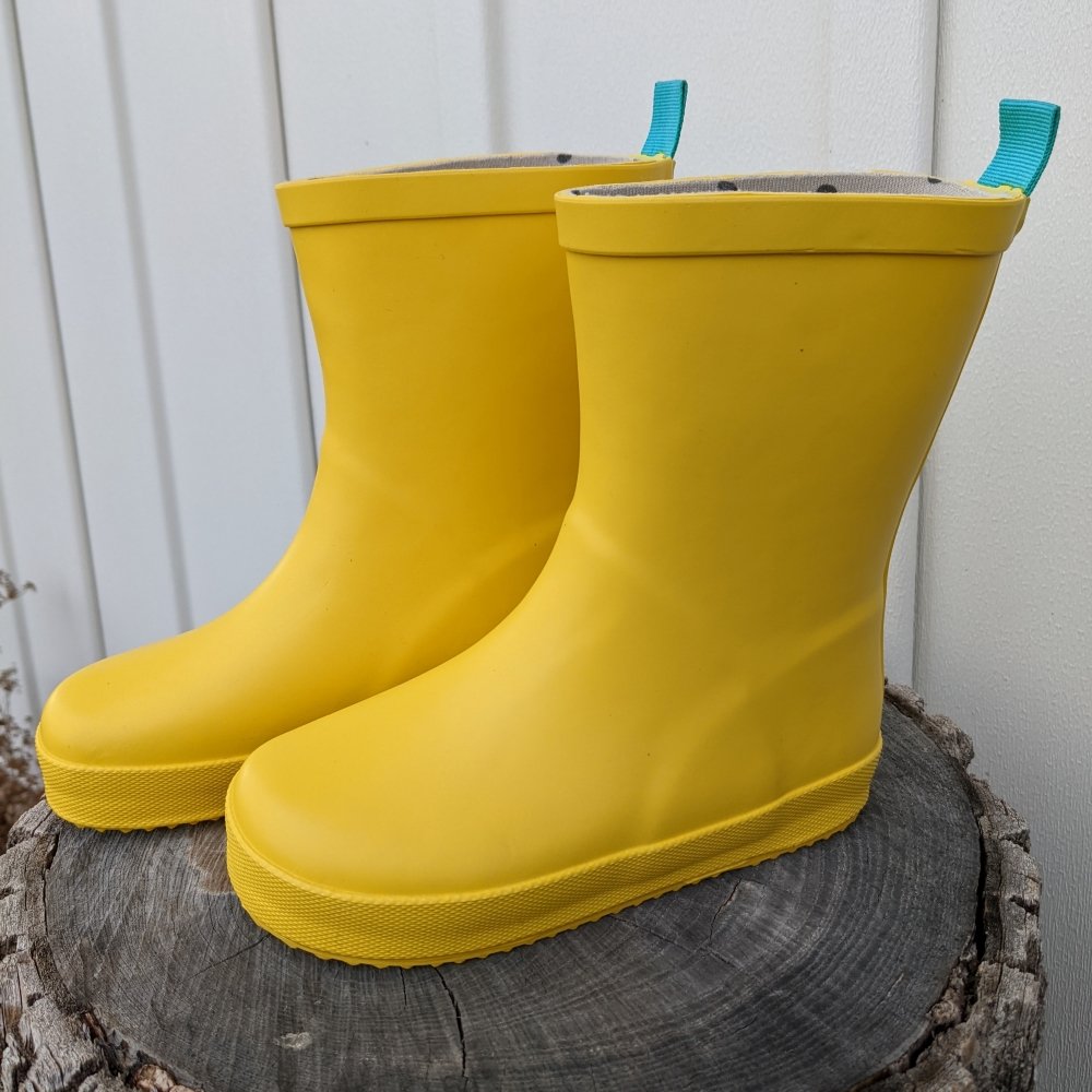 A pair of Ten Little Kids affordable yellow rain boots sitting unworn on a tree stump