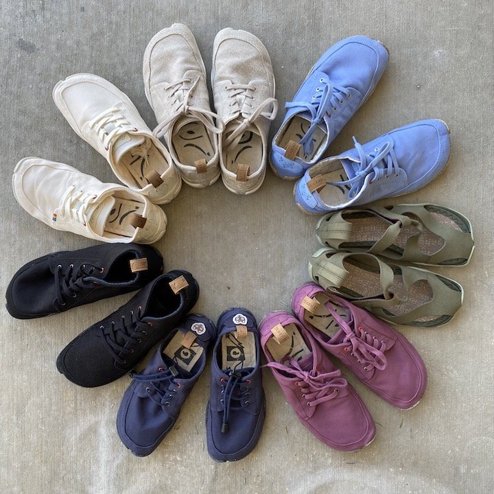 A top down view of a circle of 7 pairs of Wildling Shoes from the Spring Summer 2022 Collection in purple, green, blue, white, and black