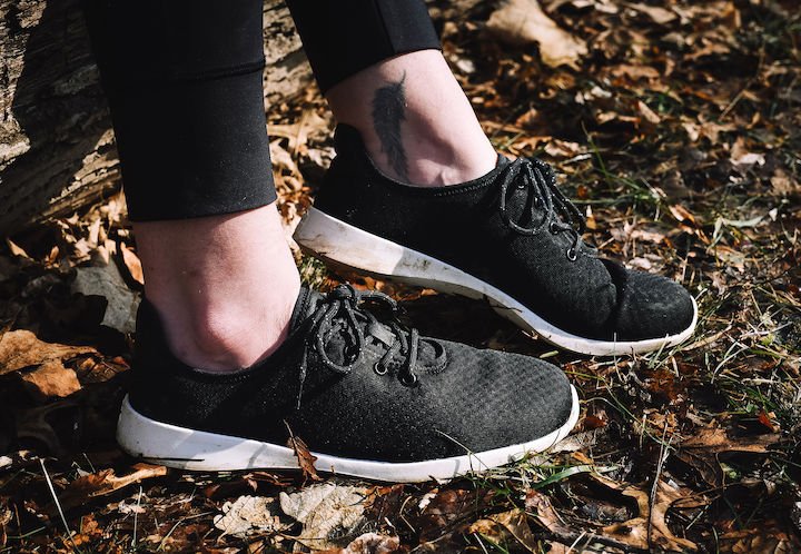 A side view of a pair of feet outside on grass wearing Groundies Performance Balance barefoot sneakers in black